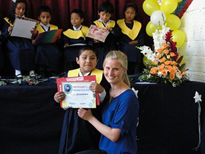 Renae Regehr poses with kindergarten graduate Ruth, who lives with her parents in prison in Bolivia. Renae and her husband Tyler are working with prison families in Bolivia, serving with MCC. The other children in the photo are Jocelyn, Luis Mario, Deymar, Brian, and Alejandra. Photo: MCC BC