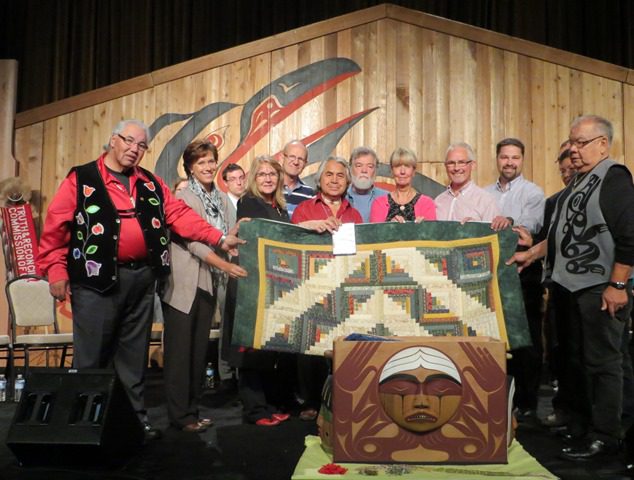 Mennonites offered an expression of reconciliation to their Aboriginal neighbours at the Truth and Reconciliation Commission's sixth National Event, Sept. 18-21, in Vancouver. The commission's mandate is to gather stories and raise awareness about the impacts of the residential school system on Aboriginal Peoples in Canada.   Representatives from the Mennonite community presented a quilt with a log cabin design as a symbol of warmth, friendship, healing, and peace. One Canadian frontier woman summarized the significance of these blankets: "I make them warm to keep my family from freezing; I make them beautiful to keep my heart from breaking."   Residential school survivor Isadore Charters (centre, in red), also gifted a copy of his 28-minute documentary Yummo Comes Home, which chronicles his story of healing and encounter with Jesus (www.outreach.ca).   Presenters included Dave Heinrichs of Eagle Ridge Bible Fellowship, Don Klaassen of Sardis Community Church, and Garry Janzen of Mennonite Church Canada. All expressions of reconciliation received during the seven national TRC events and placed in the ceremonial Bentwood Box will be permanently housed at the National Research Centre at the University of Manitoba.-LK